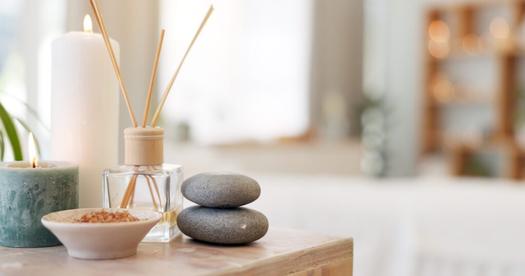 Two smooth stones stacked with a reed diffuser on a wooden surface.